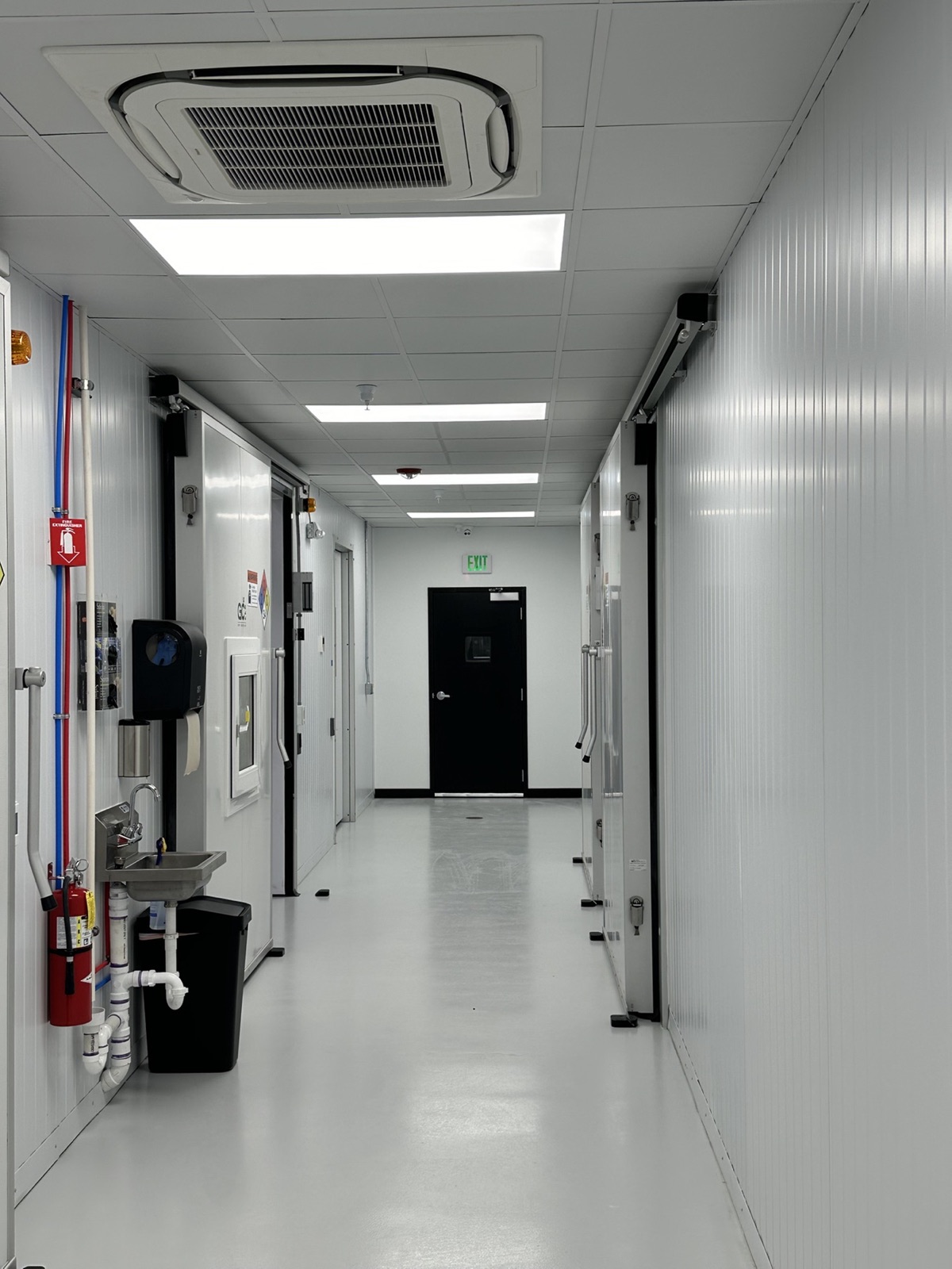 Clean controlled-environment facility corridor with production room doors, sanitation station, and compliance infrastructure